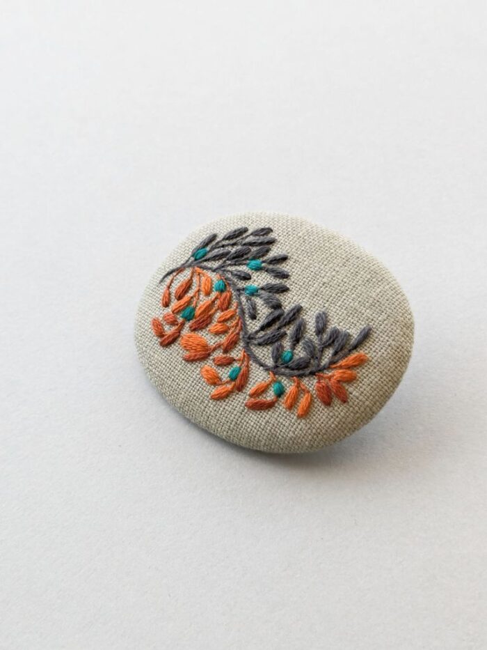 Broche textile brodée à l'aiguille d'une branche de fleurs